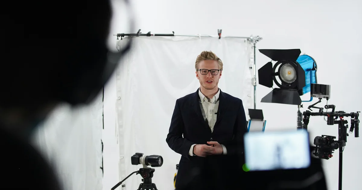Presenter in a suit filmed in a studio with lights and a camera on a tripod
