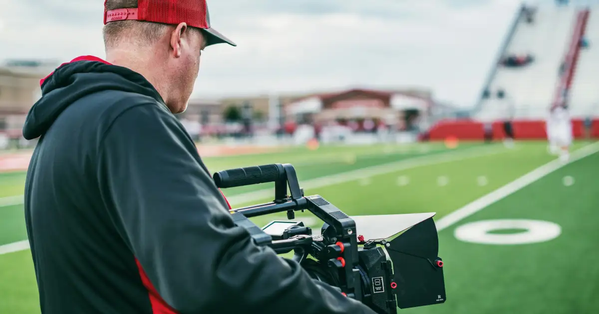 Camera operator filming a football match from the sideline