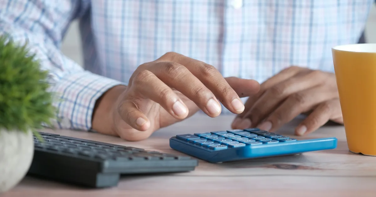 Hands working a blue calculator next to a keyboard